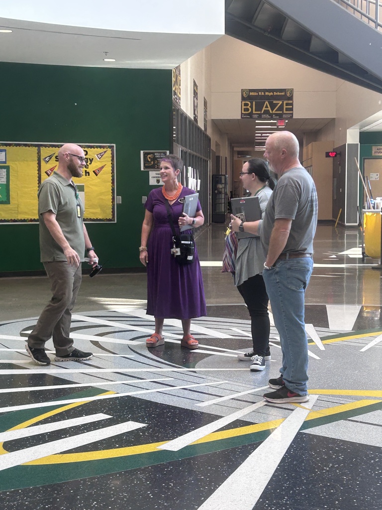 A group of people standing in a hallway with a sign for "Blaze" on the wall and yellow and black stripes on the floor.