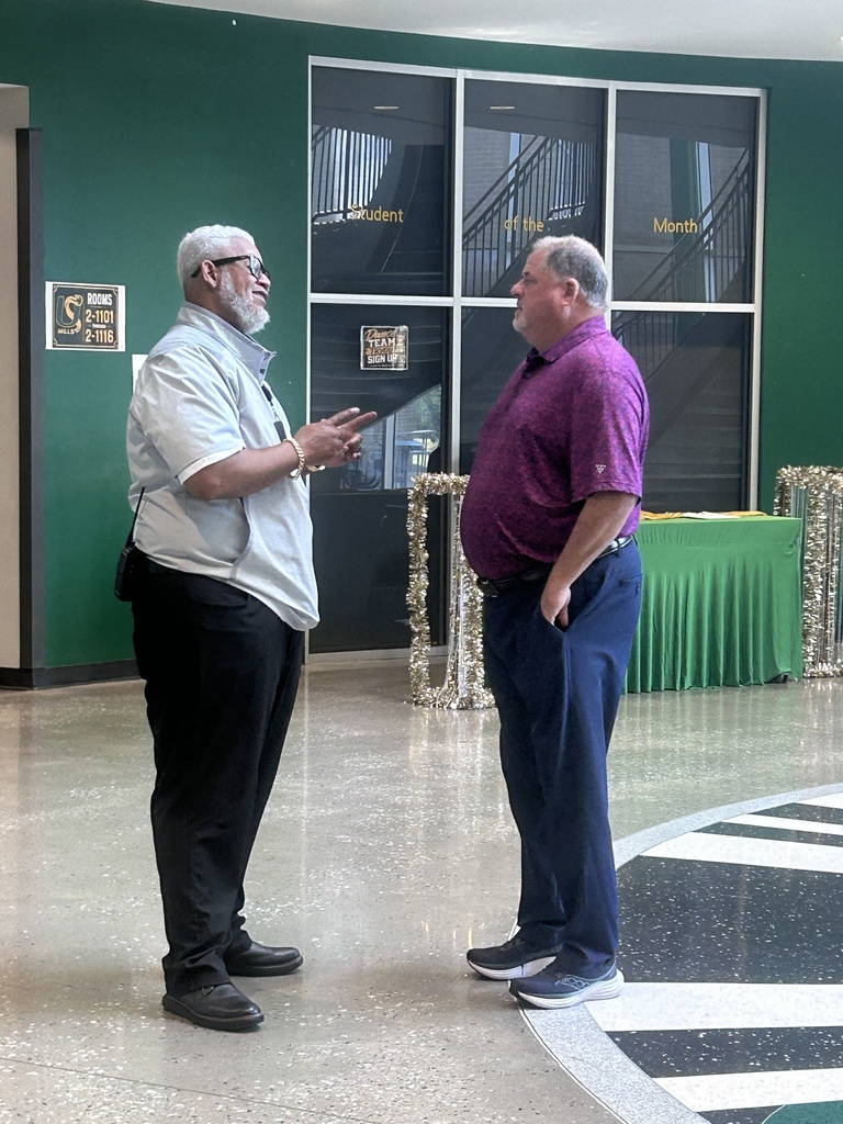 Two men in casual attire engaged in conversation in a school hallway.