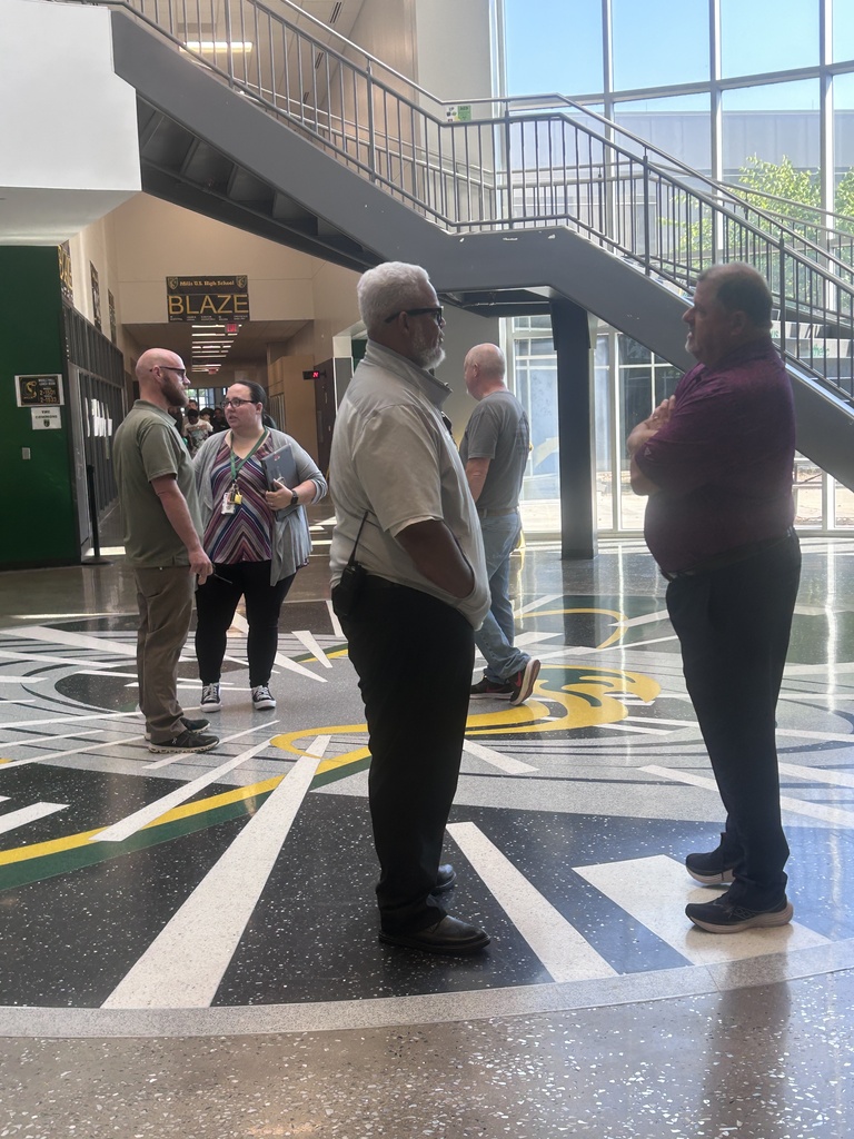 Several people standing in a lobby with a colorful floor pattern, stairs, and glass walls.