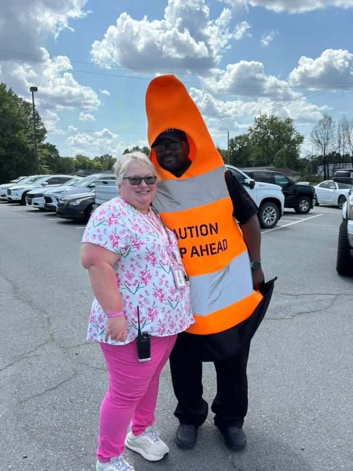 Two people, one dressed as a traffic cone smiling for the camera.