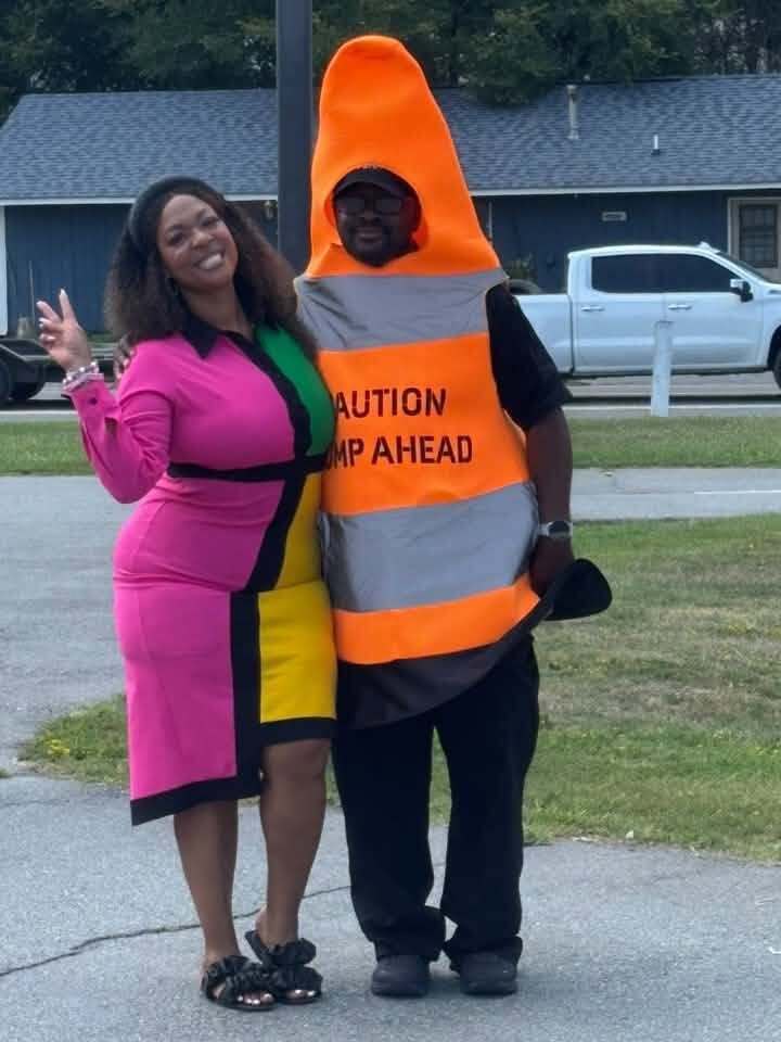 Two people, one dressed as a traffic cone smiling for the camera.