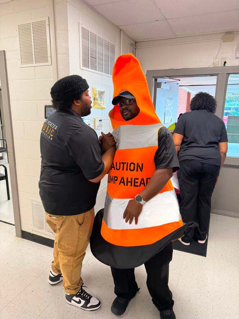 A man in a traffic cone costume getting a handshake from another man.