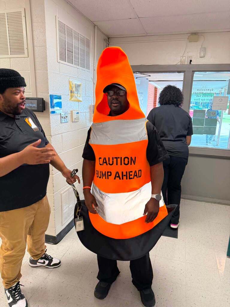 A man in a traffic cone costume speaking with another man.