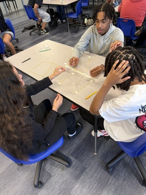 Students building a tower out of spaghetti noodle and marshmallows on a classroom table.