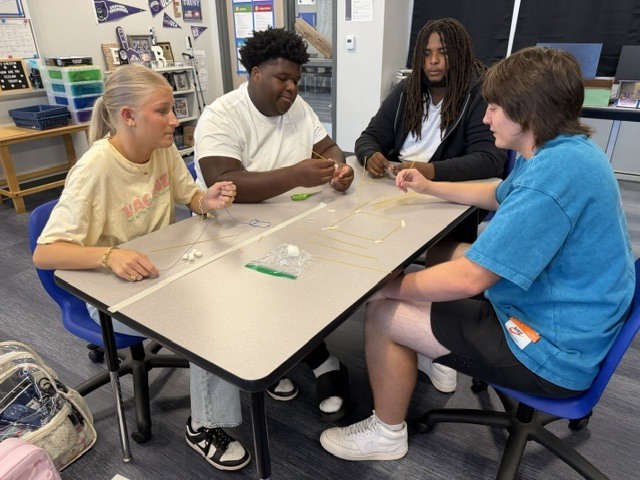 Students building a tower out of spaghetti noodle and marshmallows on a classroom table.