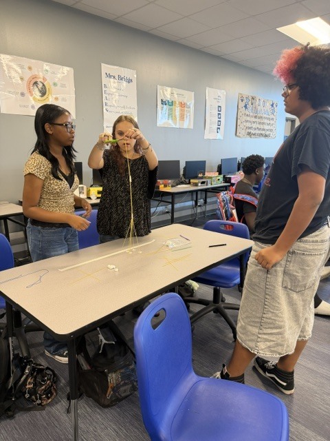 Students building a tower out of spaghetti noodle and marshmallows on a classroom table.