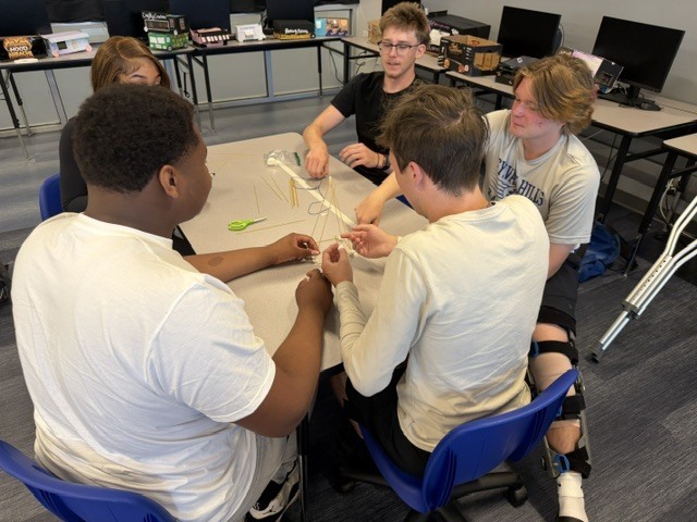 Students building a tower out of spaghetti noodle and marshmallows on a classroom table.