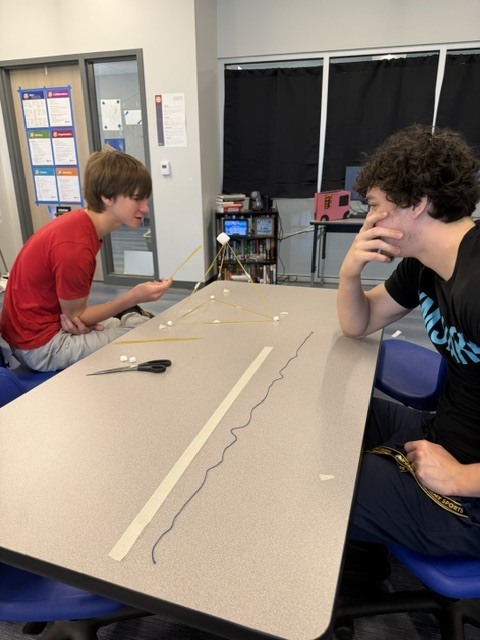 Students building a tower out of spaghetti noodle and marshmallows on a classroom table.