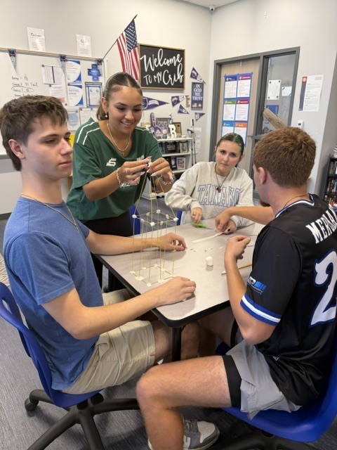 Students building a tower out of spaghetti noodle and marshmallows on a classroom table.