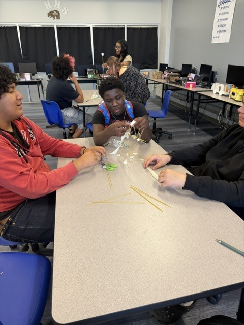 Students building a tower out of spaghetti noodle and marshmallows on a classroom table.