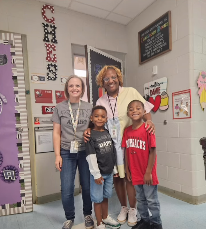 Four people wearing college shirts in a classroom.