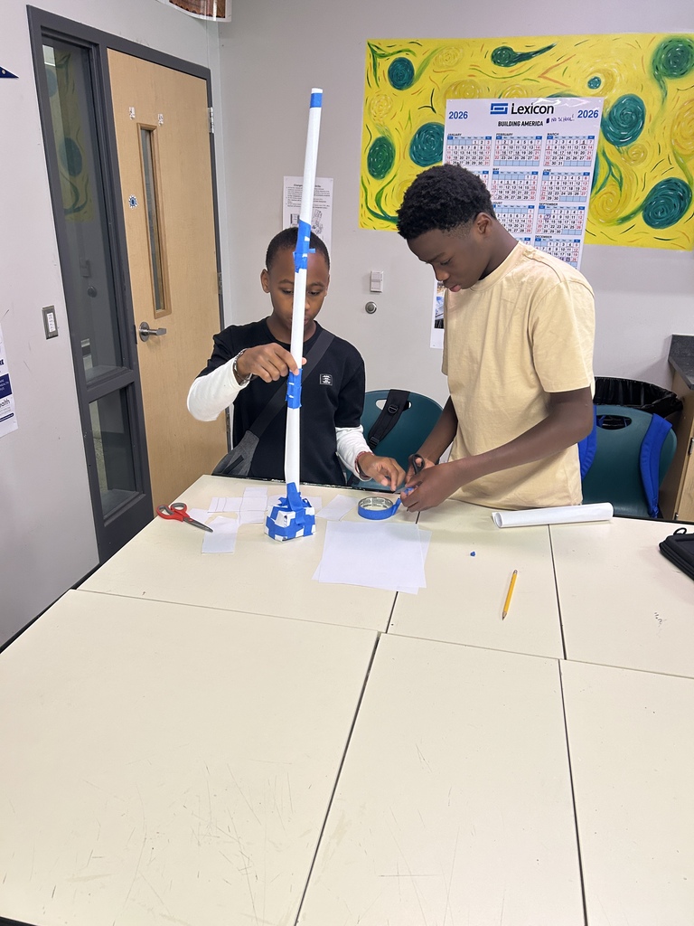 Two students building a sculpture out of printer paper and painters tape
