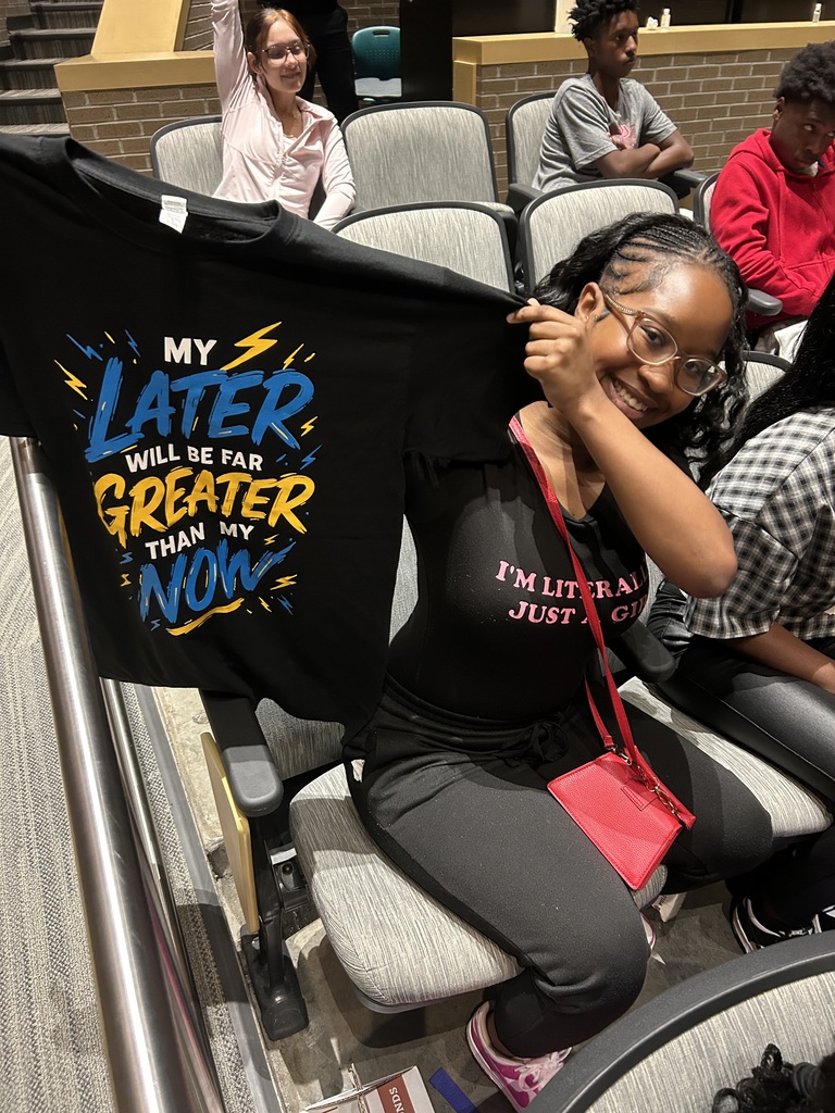 Student holding up a Tshirt that says "my later will be great than my now."