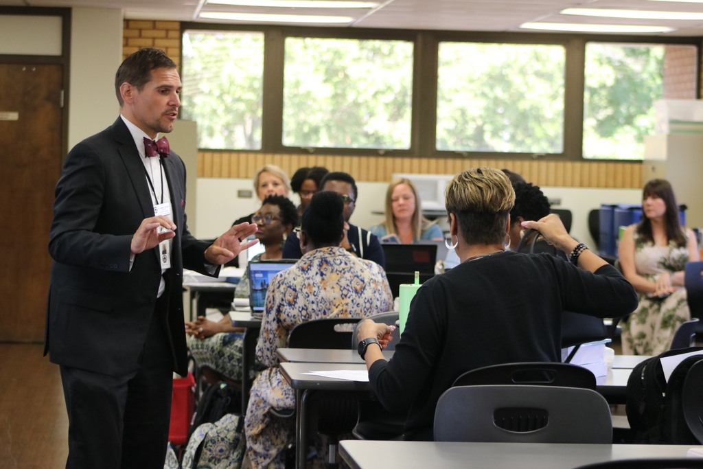 a man in a bow tie speaking to a room of principals
