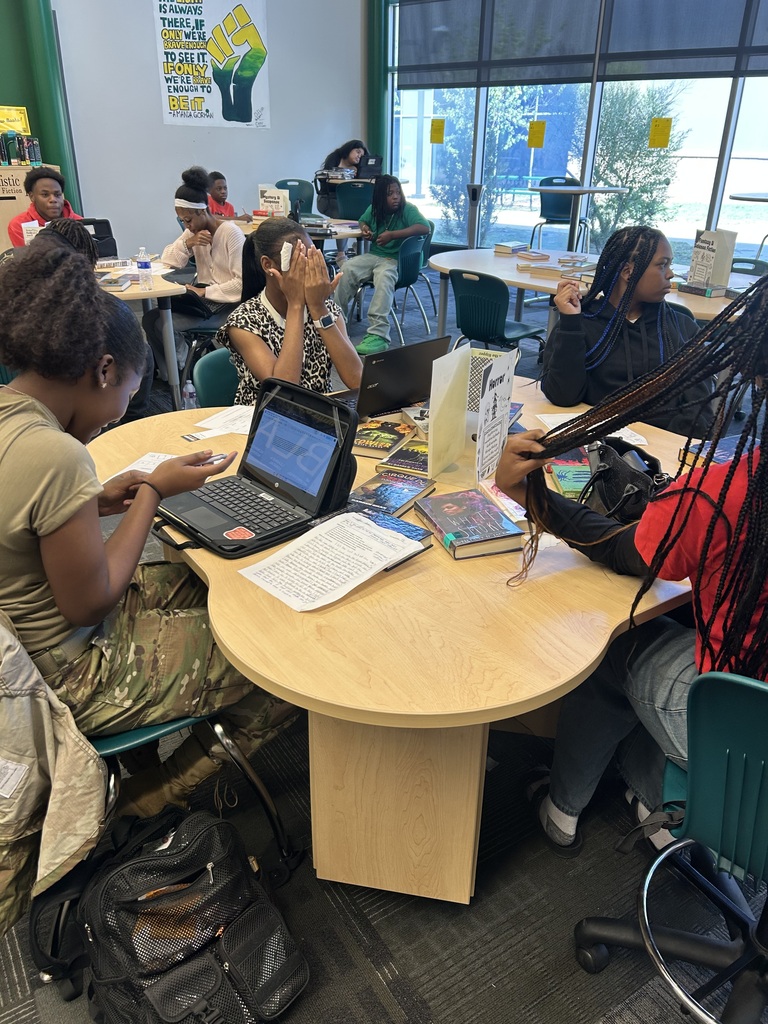 Students at library tables listening to the media specialist about books