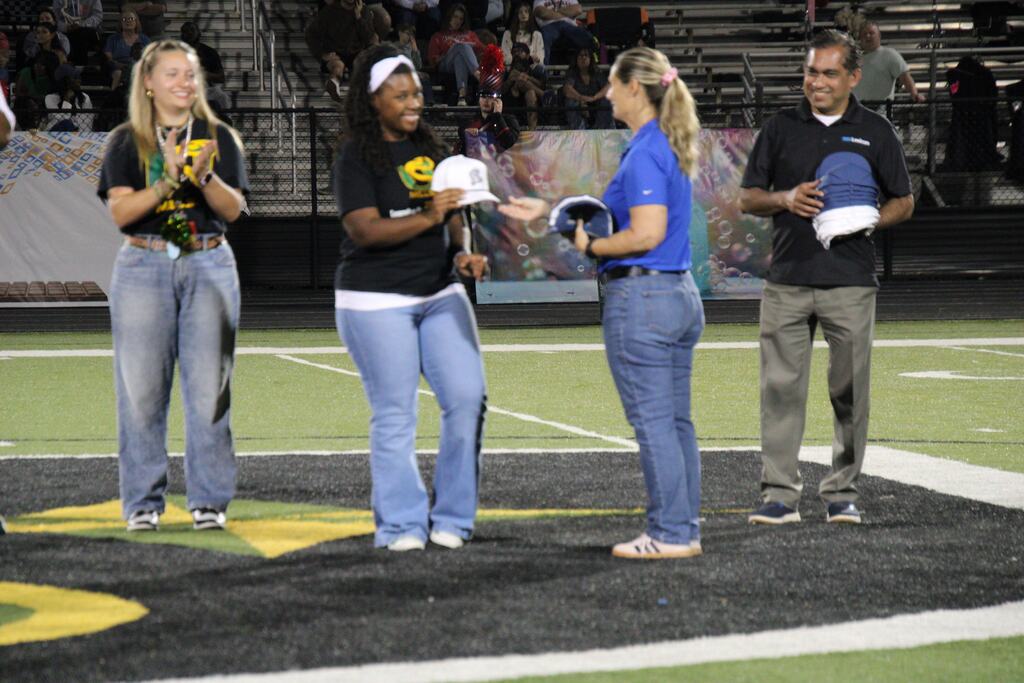 A representative presents a commemorative cap during Lexicon Academy Night as educators and industry partners participate in the recognition ceremony on the football field.