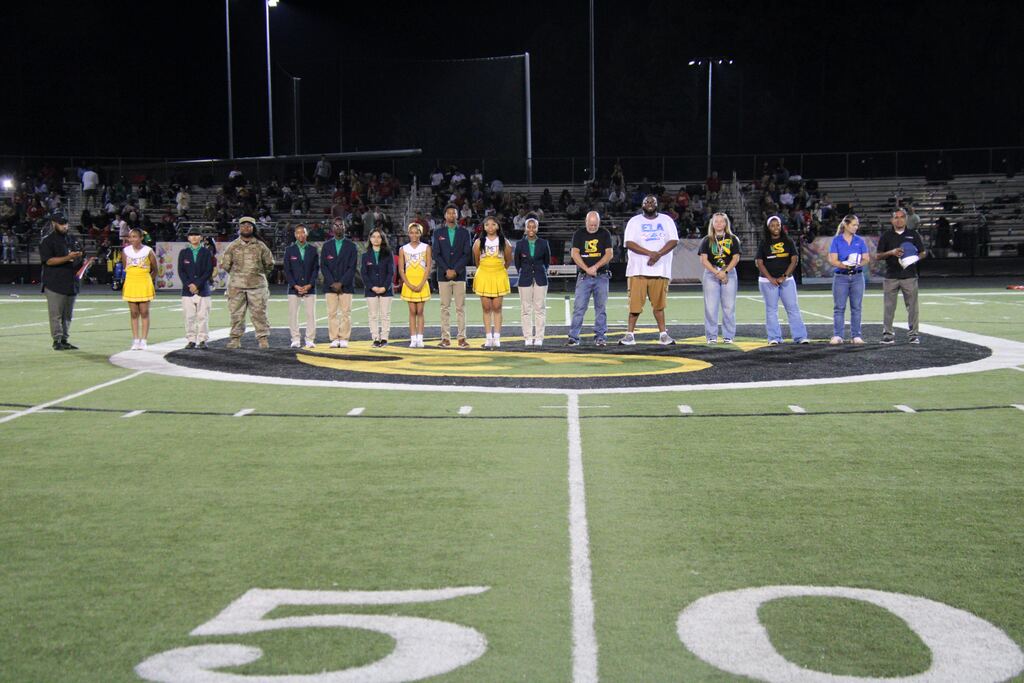 Students and representatives participating in Lexicon Academy Night stand on the football field during a recognition ceremony at Mills University Studies High School.