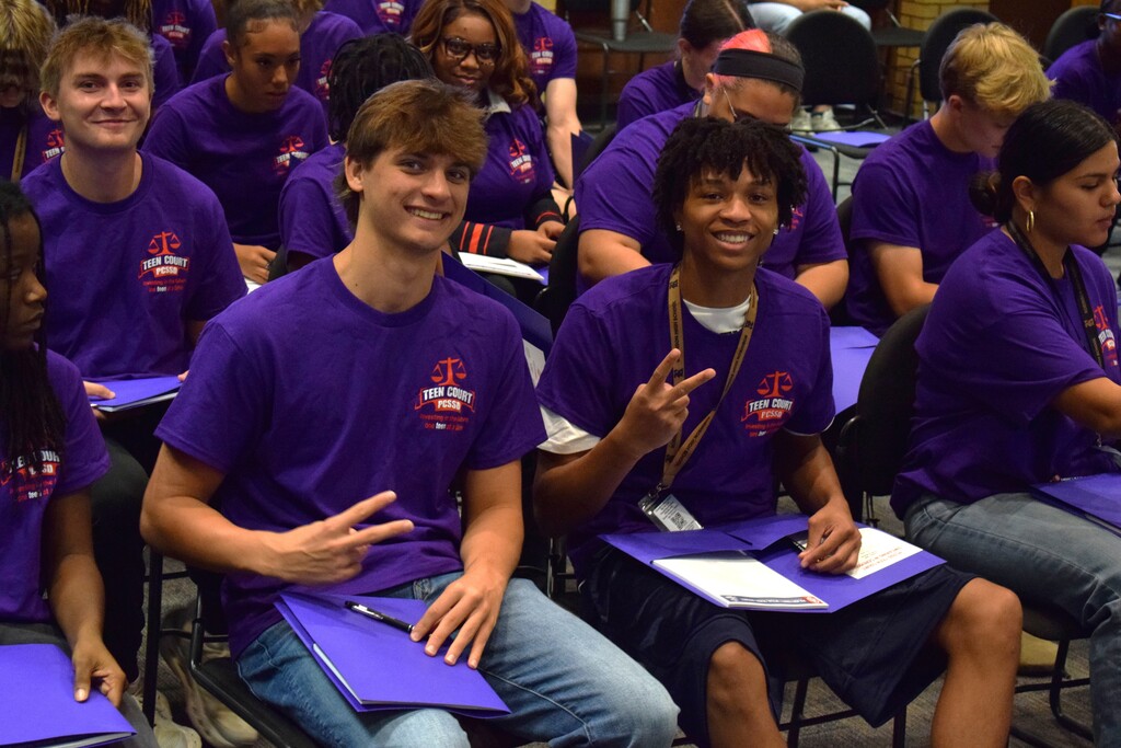 Students smiling while sitting down in teen court shirts