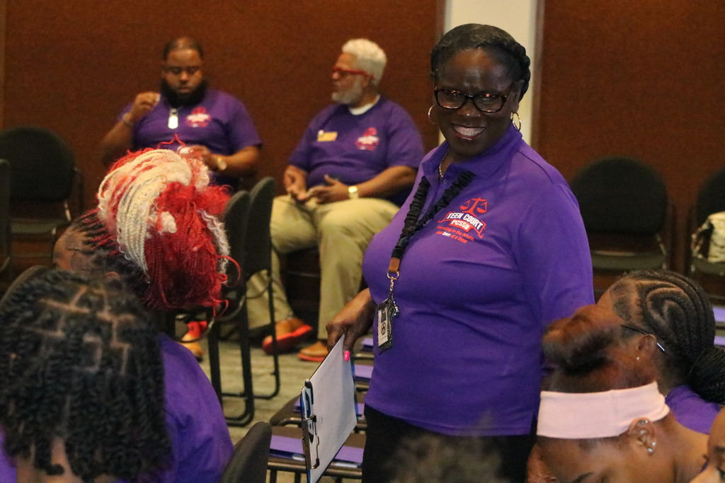 An administrator smiles at students while. Other adults are sitting in the background.