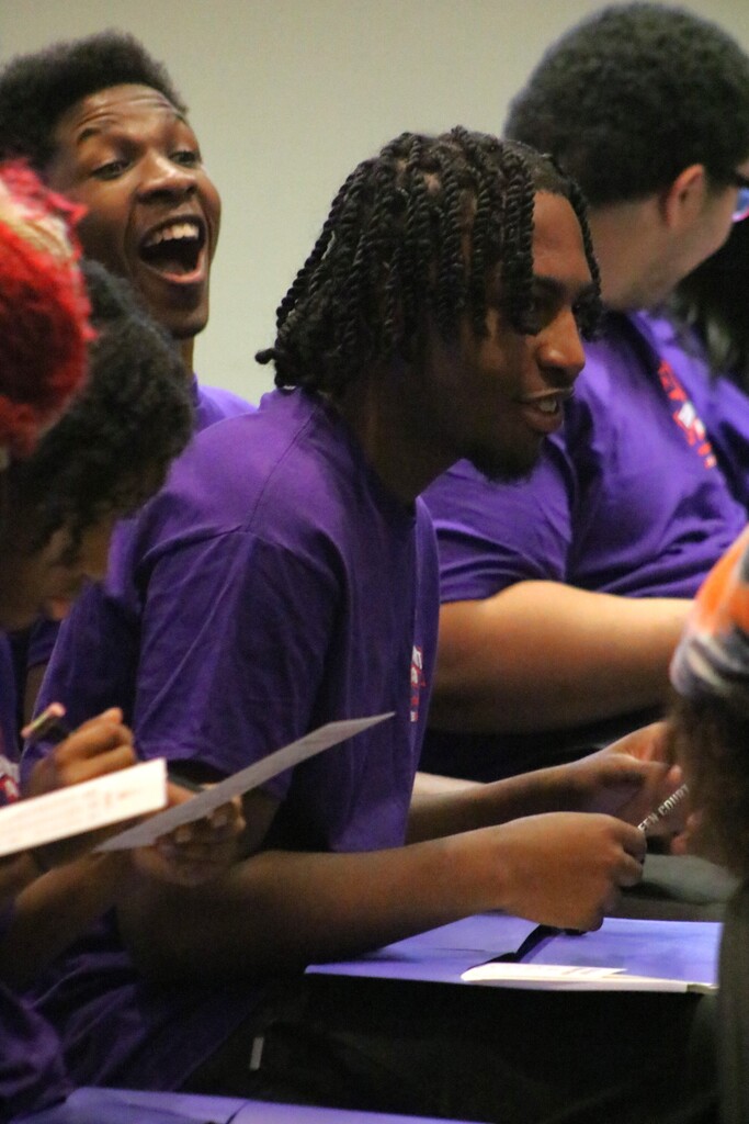 Students smiling while sitting in rows holding pencils.