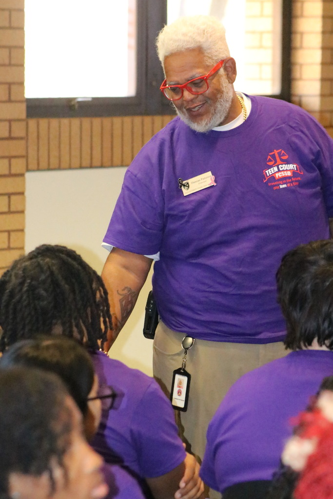 an older man wearing red glasses smiling at a younger man who is sitting down.