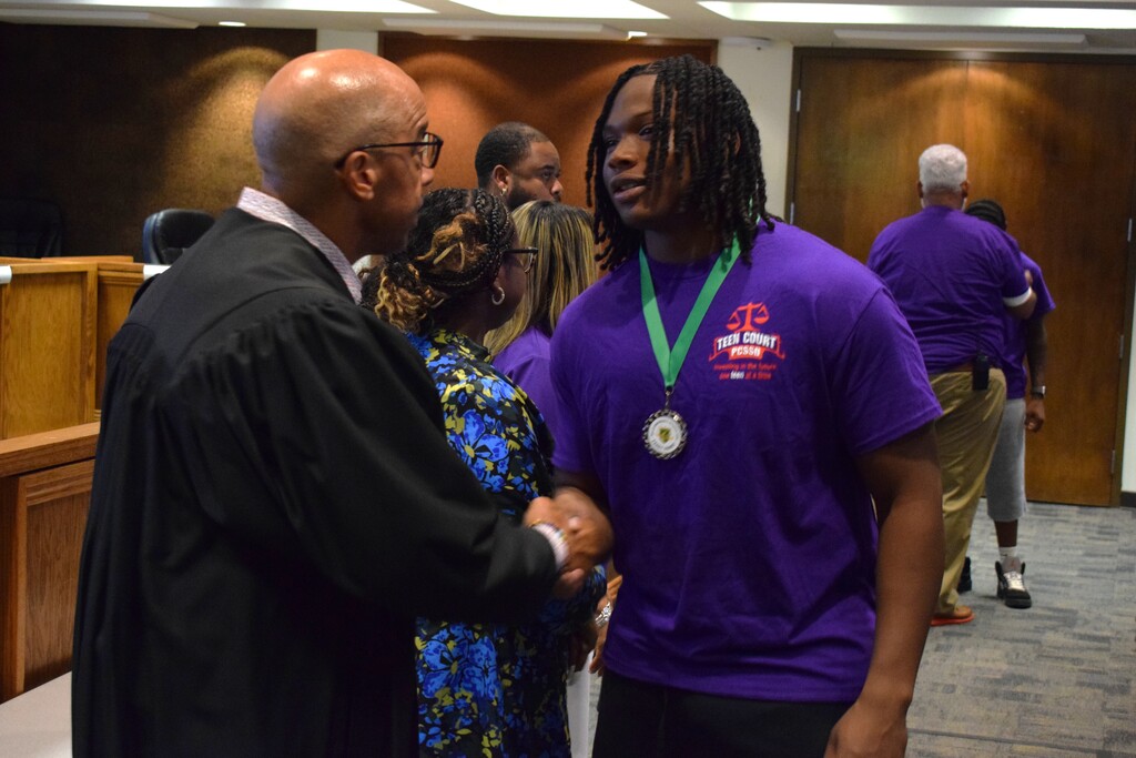 A student wearing a medal shaking the hand of a judge