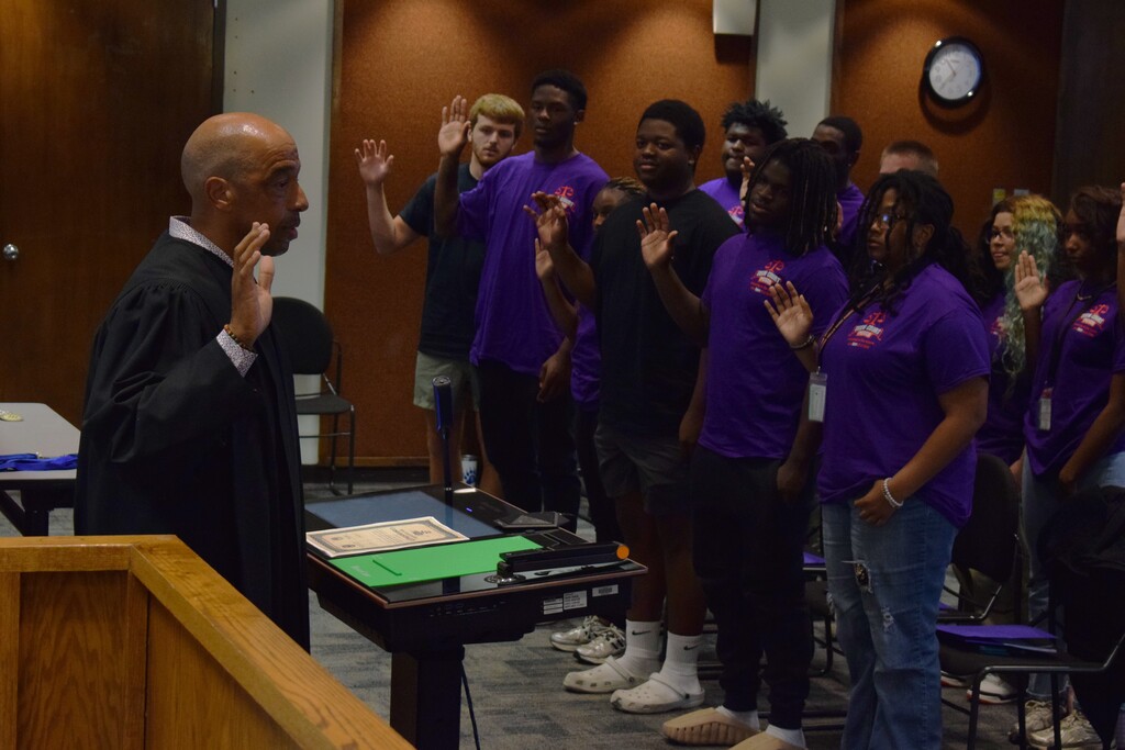 Students take a pledge standing in a board room. A judge is officiating