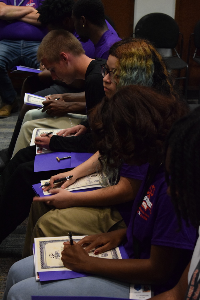 Multiple students signing a paper within a notebook