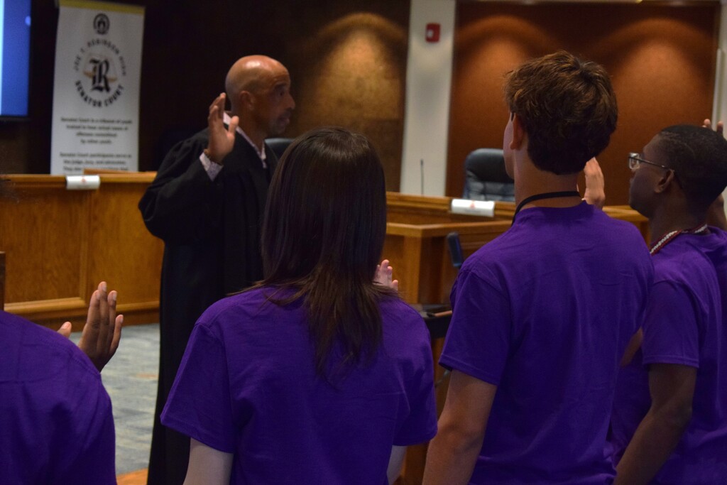 Students raising their hands in a pledge with a judge administering it.