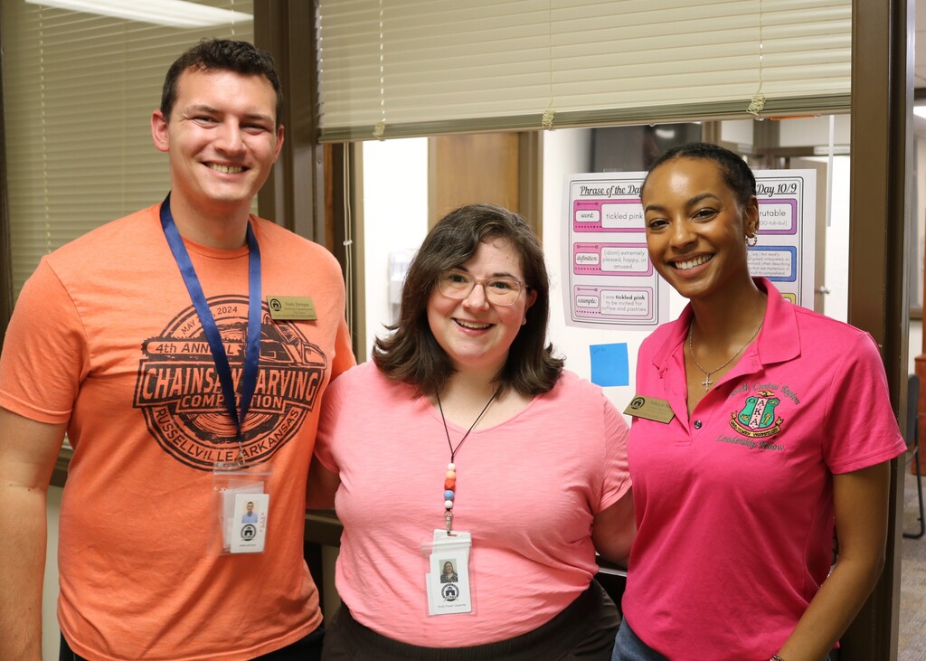 Three Pulaski County Special School District employees pose together in an office area wearing shades of pink and coral in support of Breast Cancer Awareness Month.