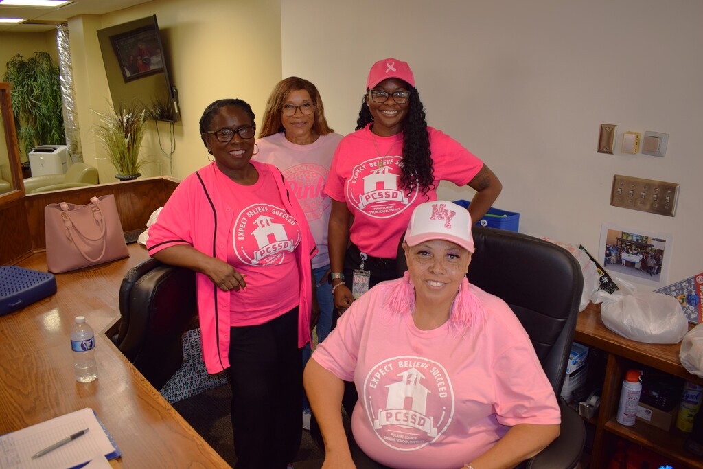 Three Pulaski County Special School District employees pose together at the front desk wearing shades of pink in support of Breast Cancer Awareness Month.