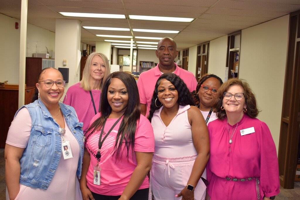 Seven Pulaski County Special School District employees gather in a hallway wearing pink and light pink clothing for Breast Cancer Awareness Month.