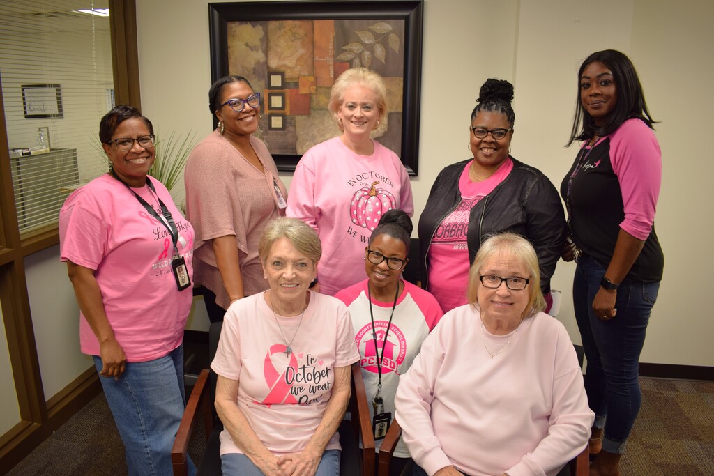 Eight Pulaski County Special School District employees gather for a group photo in an office lobby wearing pink clothing and breast cancer awareness shirts for Pink Out Day.