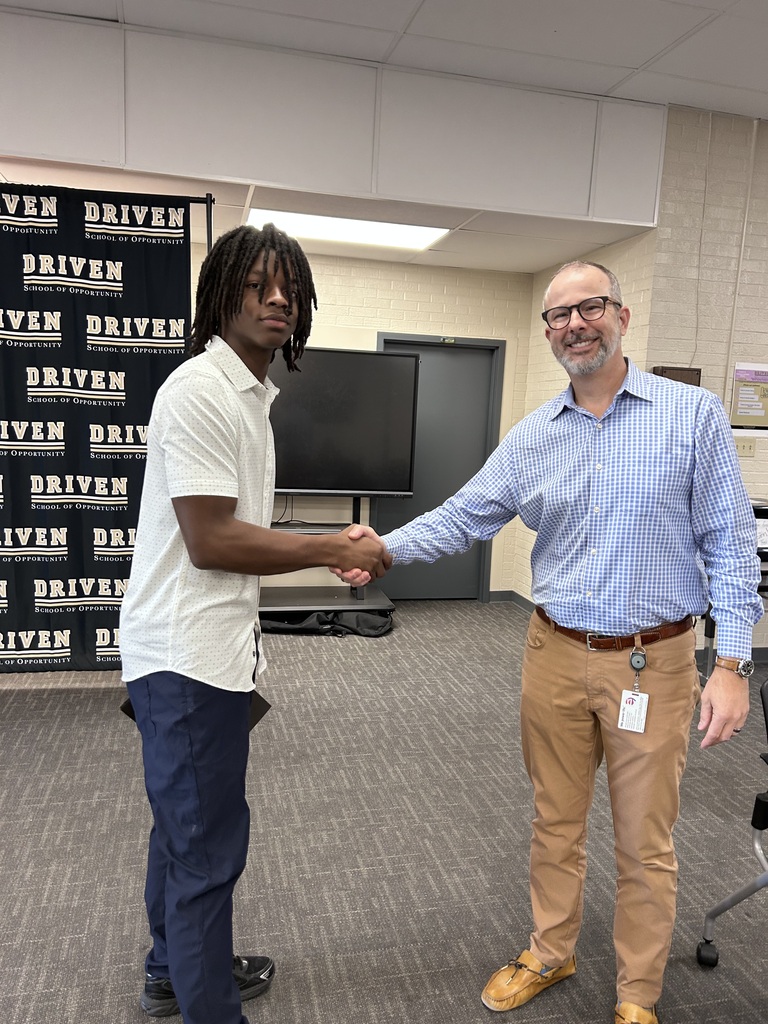 A student and adult handshake with a DRIVEN backdrop