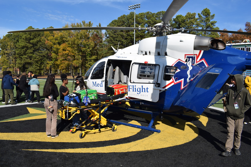 Students look at a gurney and a helicopter at a football stadium.