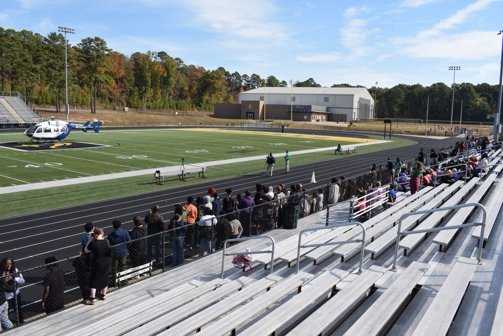 students watch from bleachers and a track a helicopter preparing to take off