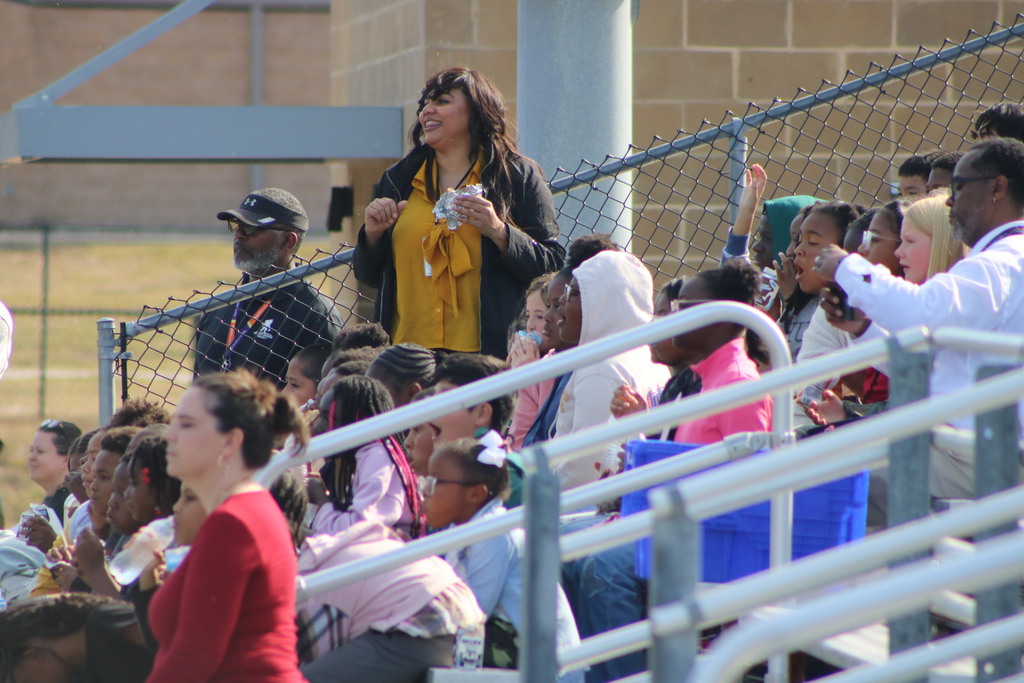 A teachers smiles with her students around her sitting down in bleachers