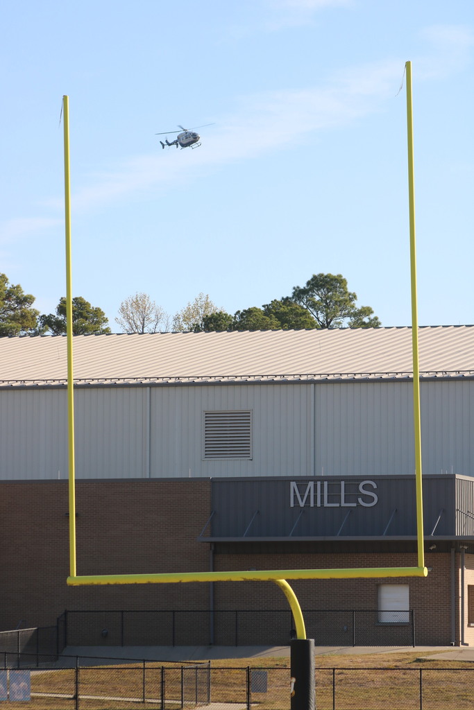 a helicopter descends beyond a goal post and a building that says MILLS