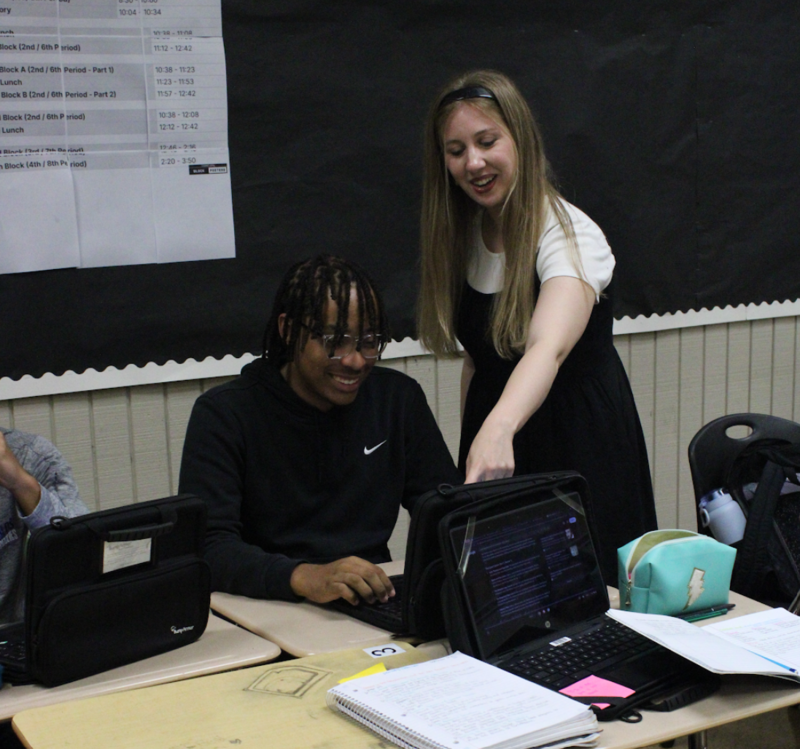 Rachel Farhat standing in front of a powerpoint presentation in a classroom teaching her journalism students excellence in journalism at Joe T. Robinson High School. Students are in the foreground  looking toward her or their laptops.