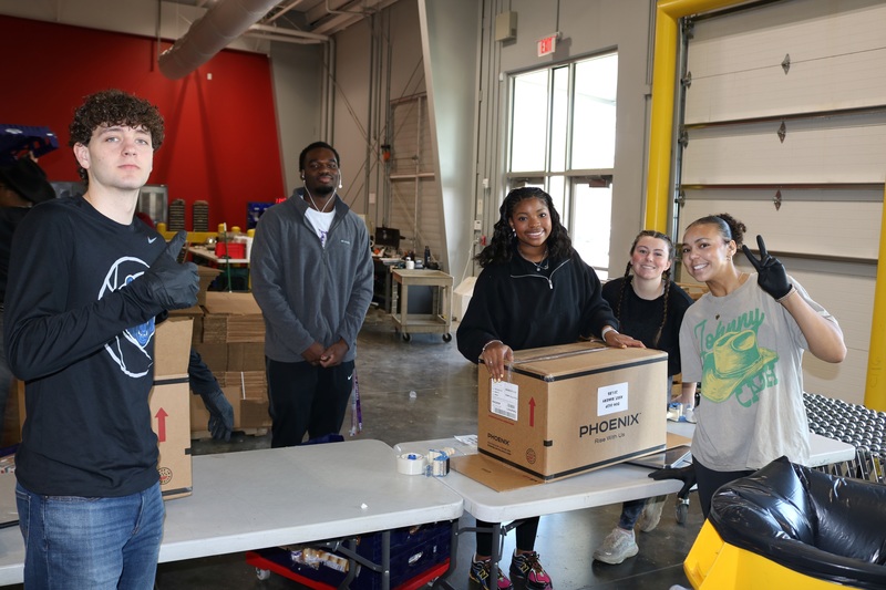Five students smiling as they pack a box at the AR Foodbank