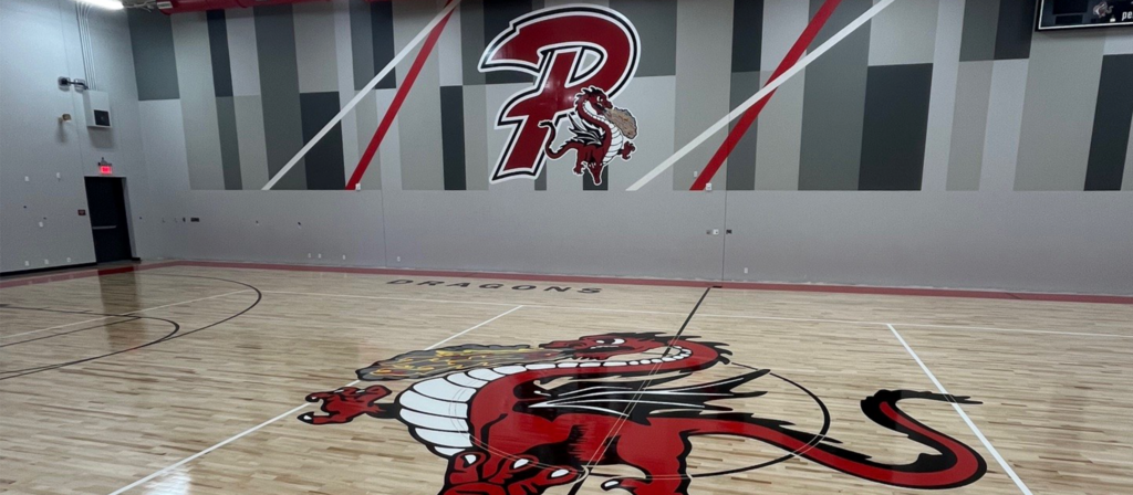 Picture of the Junior High gym interior with a picture of the Dragon logo on the gym floor and the graphics on the wall.
