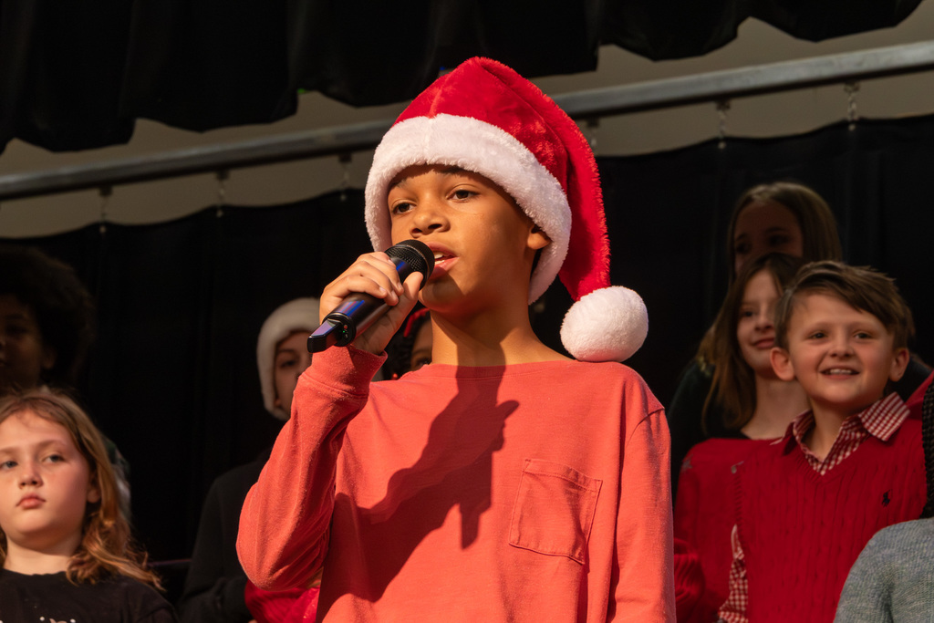 Elementary student singing at microphone wearing Santa hat