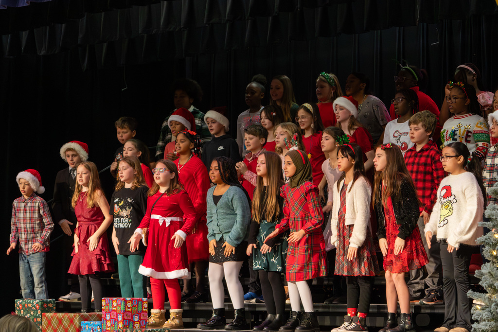 Elementary choir singing and dancing on risers, wearing holiday attire