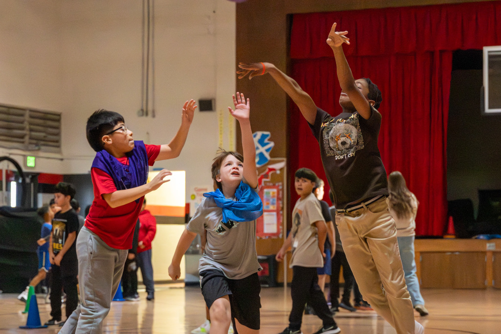 One middle school student shoots the ball as two opponents stretch their arms out to defend