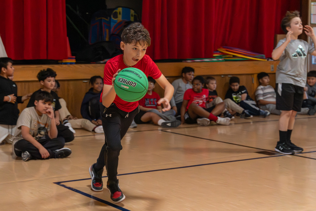 Middle school student dribbles down a gym baseline