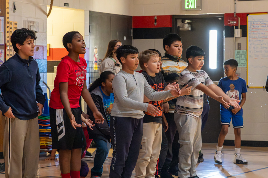 Middle school students stand huddled on a gym baseline and cheer