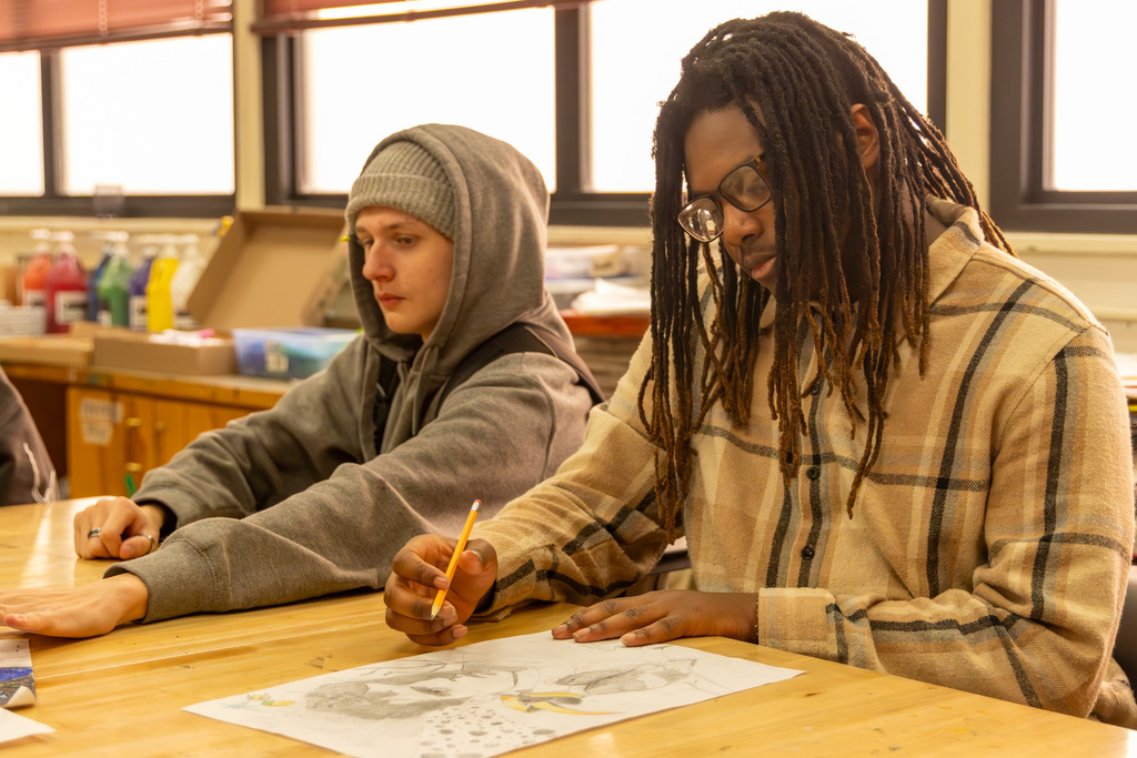 Two students seated at a wooden desk drawing