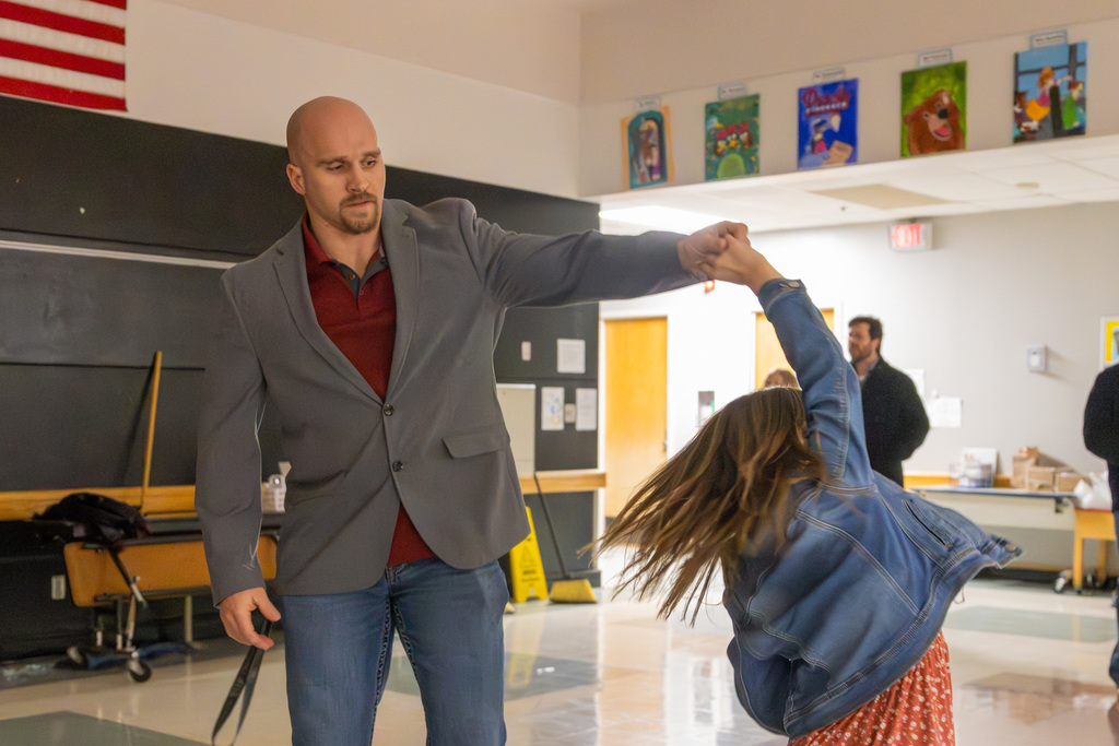 A man in a suit jacket spins a girl in a red polka-dot dress