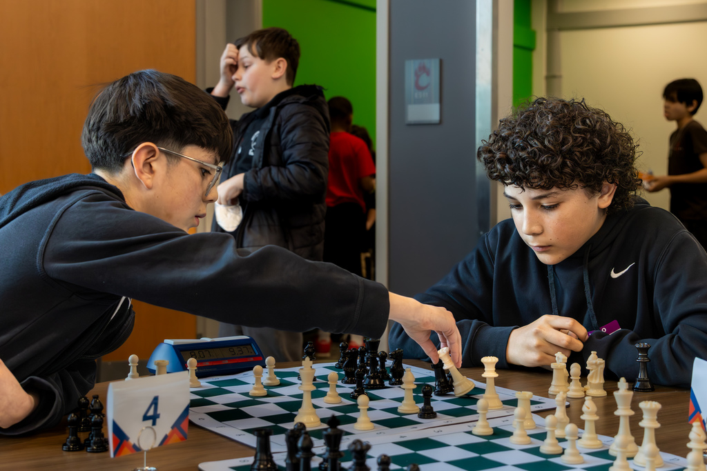 Boy reaching across a table to move a chess piece