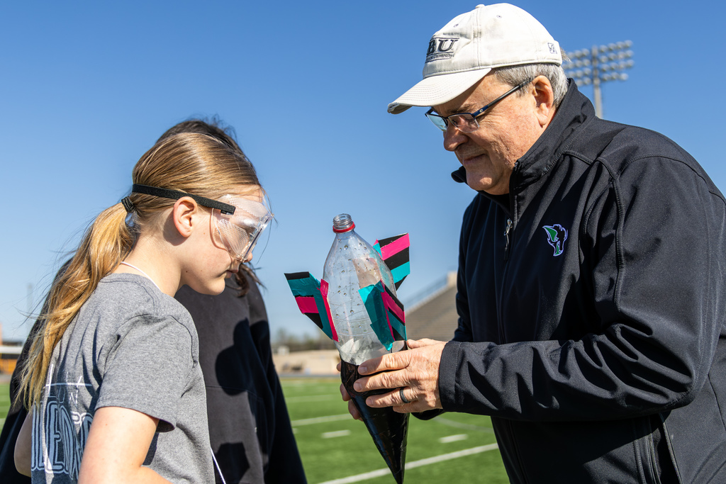 a student and teacher looking intently at a bottle rocket